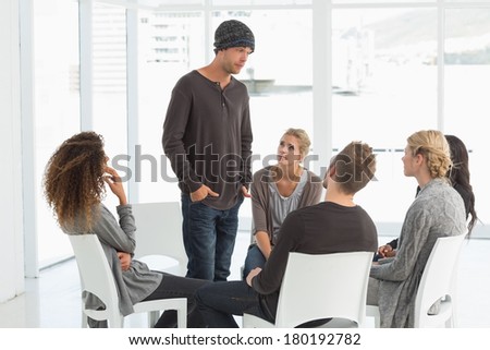Rehab group listening to man standing up introducing himself at therapy session