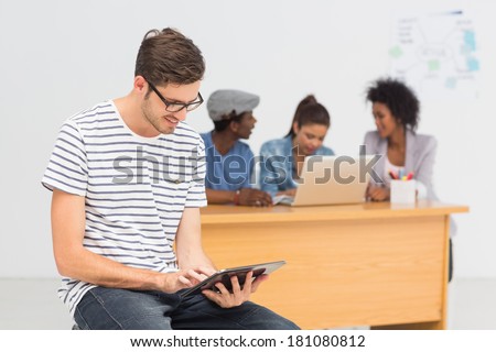 Casual male artist using digital tablet with colleagues in the background at a bright office