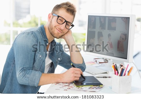 Handsome editor working with graphics tablet smiling at camera in creative office