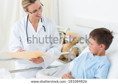 Happy female doctor examining report of sick boy in hospital