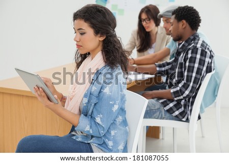 Side view of a woman using digital tablet with group in meeting at office