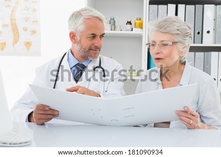 Male doctor with female patient reading reports at medical office