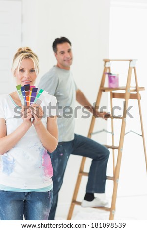 Smiling woman holding color swatches with man by ladder in a new house