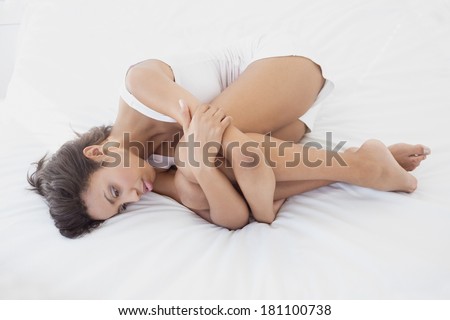 Unhappy brunette lying on her bed hugging her knees at home in the bedroom