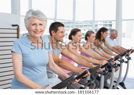 Group portrait of happy people working out at exercise bike class in gym