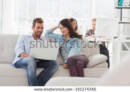 Young smiling designers working on laptop on the couch in creative office