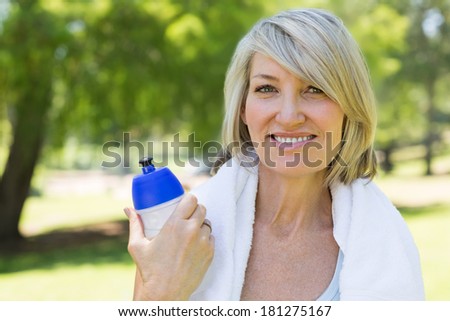 Closeup portrait of fit woman with towel around neck holding water bottle in park