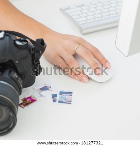 Digital camera on photographers desk with womans hand on mouse in creative office