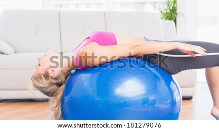 Slim blonde stretching her back on exercise ball at home in the living room