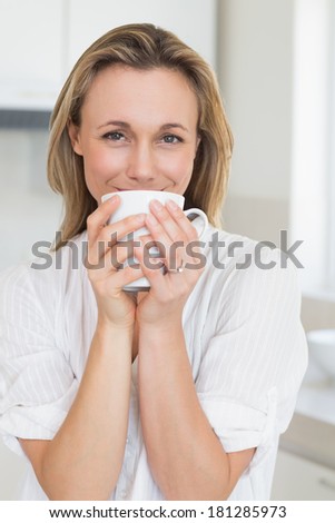 Smiling woman sitting and holding mug at home in the kitchen