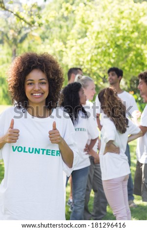 Confident female volunteer gesturing thumbs up with friends disucssing in background