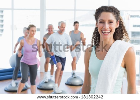 Portrait of a cheerful young woman with people exercising in the background at fitness studio