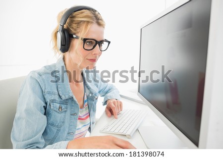 Blonde designer wearing headphones working at computer in creative office