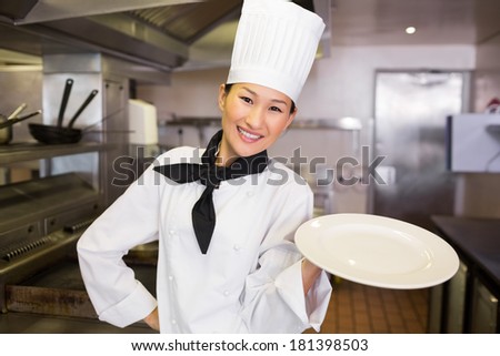 Portrait of a smiling female cook holding an empty plate in the kitchen