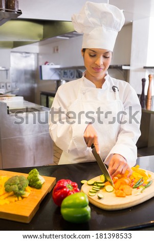 Concentrated young female chef cutting vegetables in the kitchen