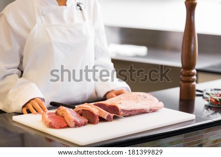 Closeup mid section of a chef with cut meat pieces in the kitchen