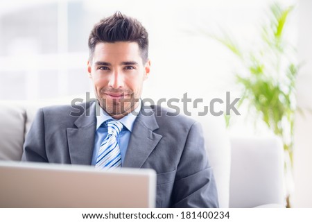 Handsome businessman sitting on sofa using his laptop in the office