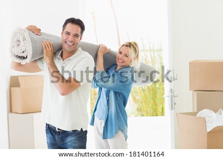 Portrait of a smiling couple carrying rolled rug after moving in a house