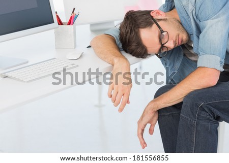 Young casual man sleeping in front of computer at a bright office
