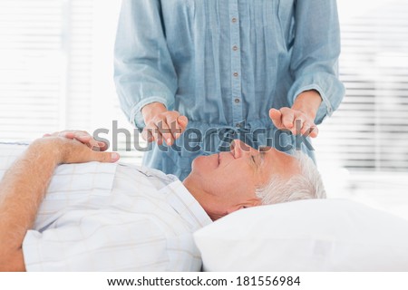 Female therapist performing Reiki over senior man at health spa