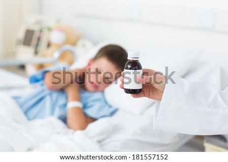 Closeup of doctor holding bottle of cough syrup with sick boy in hospital bed