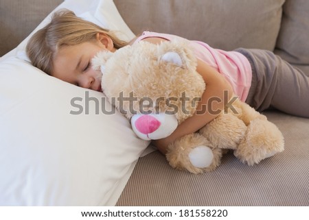 Close-up of a young girl sleeping on sofa with stuffed toy in the living room at home