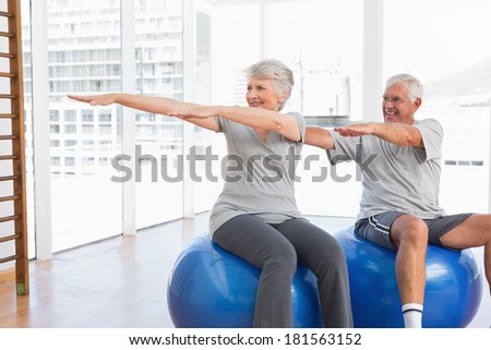 Happy senior couple doing stretching exercises on fitness balls in the medical office
