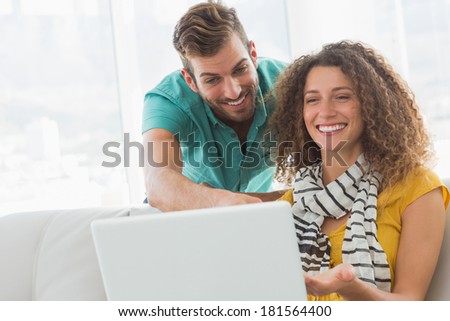 Smiling woman on the couch showing her co worker her laptop in creative office