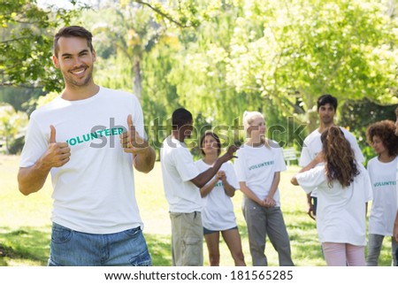 Portrait of handsome volunteer showing thumbs up with friends disucssing in background