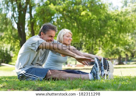 Happy couple stretching while sitting on grass in the park