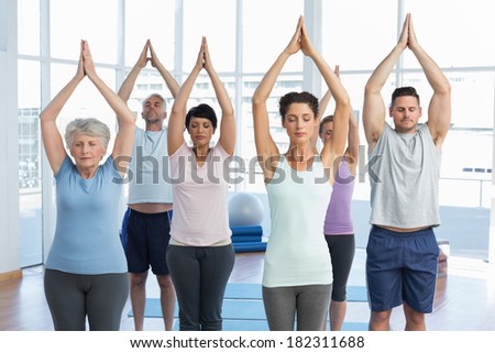 Sporty people with eyes closed and joined hands at a bright fitness studio