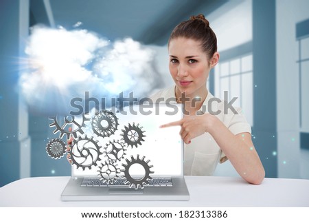 Digital composite of businesswoman pointing to her laptop showing cogs and wheels
