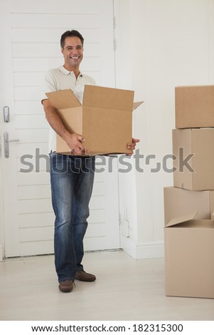 Portrait of a smiling man carrying boxes in new house