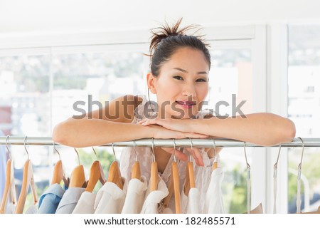 Portrait of a beautiful female fashion designer with rack of clothes in the store