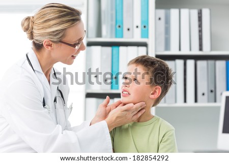 Female pediatrician examining thyroid gland of little boy in clinic