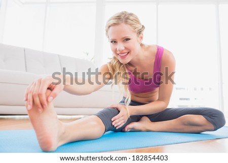 Toned blonde stretching on exercise mat smiling at camera at home in the living room