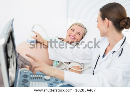 Happy female doctor showing woman her baby on ultrasound at the hospital