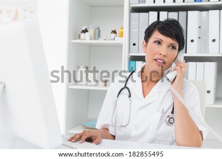Concentrated female doctor using computer and telephone at medical office