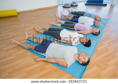 Side view of fitness class resting on mats in row at yoga class