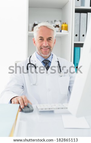 Portrait of a confident smiling male doctor sitting with computer at medical office