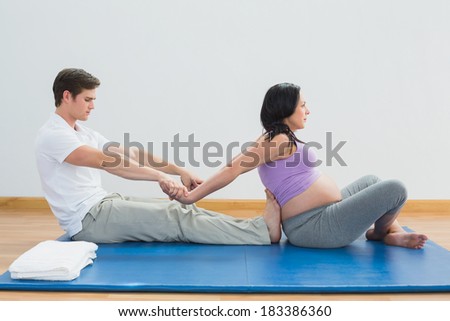Masseur stretching pregnant womans arms and shoulders on a mat in a fitness studio