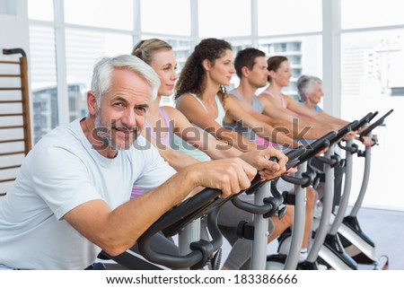 Group portrait of happy people working out at exercise bike class in gym