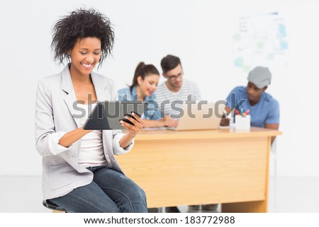 Casual female artist using digital tablet with colleagues in the background at a bright office