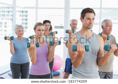 Fitness class exercising with dumbbells in a bright gym
