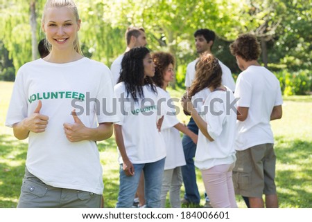 Beautiful female volunteer gesturing thumbs up with friends disucssing in background