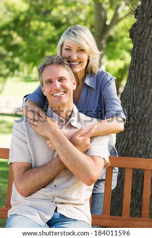 Portrait of happy woman embracing man from behind in park