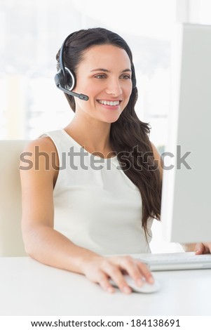 Smiling call centre agent sitting at her desk on a call in creative office