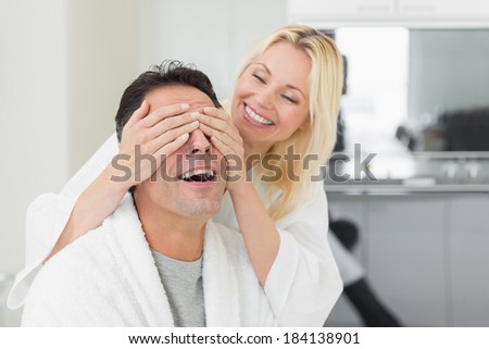 Smiling woman covering happy mans eyes in the kitchen at home