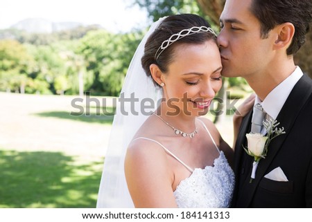 Young groom kissing shy bride on head in garden