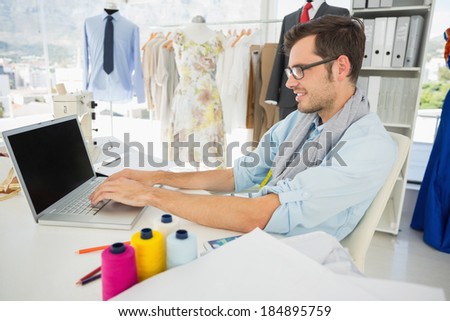 Side view of a concentrated young male fashion designer using laptop in the studio